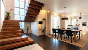 Eine moderne Küche mit dunklem Boden, einer Holztreppe und einem Essbereich mit großem Tisch und Stühlen.