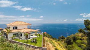 Ein Küstenhaus mit einer großen Terrasse, einem Pool und Meerblick.