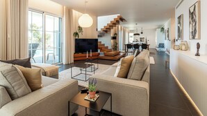 Ein modernes Wohnzimmer mit einer Couch, einem Couchtisch und einem Fernseher. Eine Treppe führt zu einer weiteren Ebene.