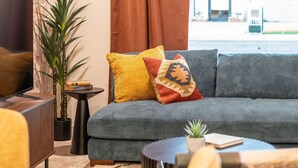 Ein modernes Wohnzimmer mit einem grauen Sofa, einem kleinen Beistelltisch, einem Blumentopf und einem Fernseher.