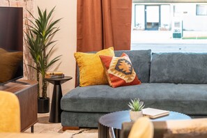 A modern living room with a grey sofa, a small side table, a potted plant, and a television. - 4 Min to Old Town, Heated Pool, Hot Tub, Firepit, Ping Pong, Sleeps 12 (Scottsdale)