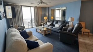 A living room with a sofa, armchair, and coffee table. There is a ceiling fan, a window with curtains, and a mirror on the wall. - 14th floor 4BR/3BA Ocean Front Condo: Stunning Views & Upgraded Ocean Bay Club (North Myrtle Beach)