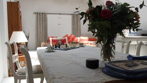 Un rincón comedor con una mesa dispuesta para tomar té, un florero con flores y vistas a un dormitorio con cama y cortinas.