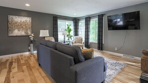 Ein modernes Wohnzimmer mit grauem Sofa, einem Couchtisch und einem an der Wand befestigten Fernseher.