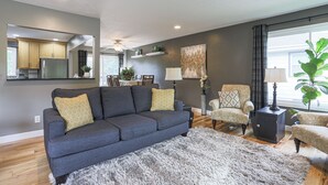 Ein modernes Wohnzimmer mit einem grauen Sofa, einem gemusterten Sessel und einem flauschigen Teppich.