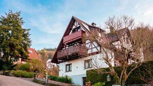 Ein traditionelles Fachwerkhäuschen mit einem steilen Satteldach, einem Balkon und einem gepflegten Garten.