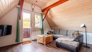 Ein Loft-Zimmer mit Holzbalkendecke, einer Couch, einem Couchtisch, einem Fernseher und einer Lampe.