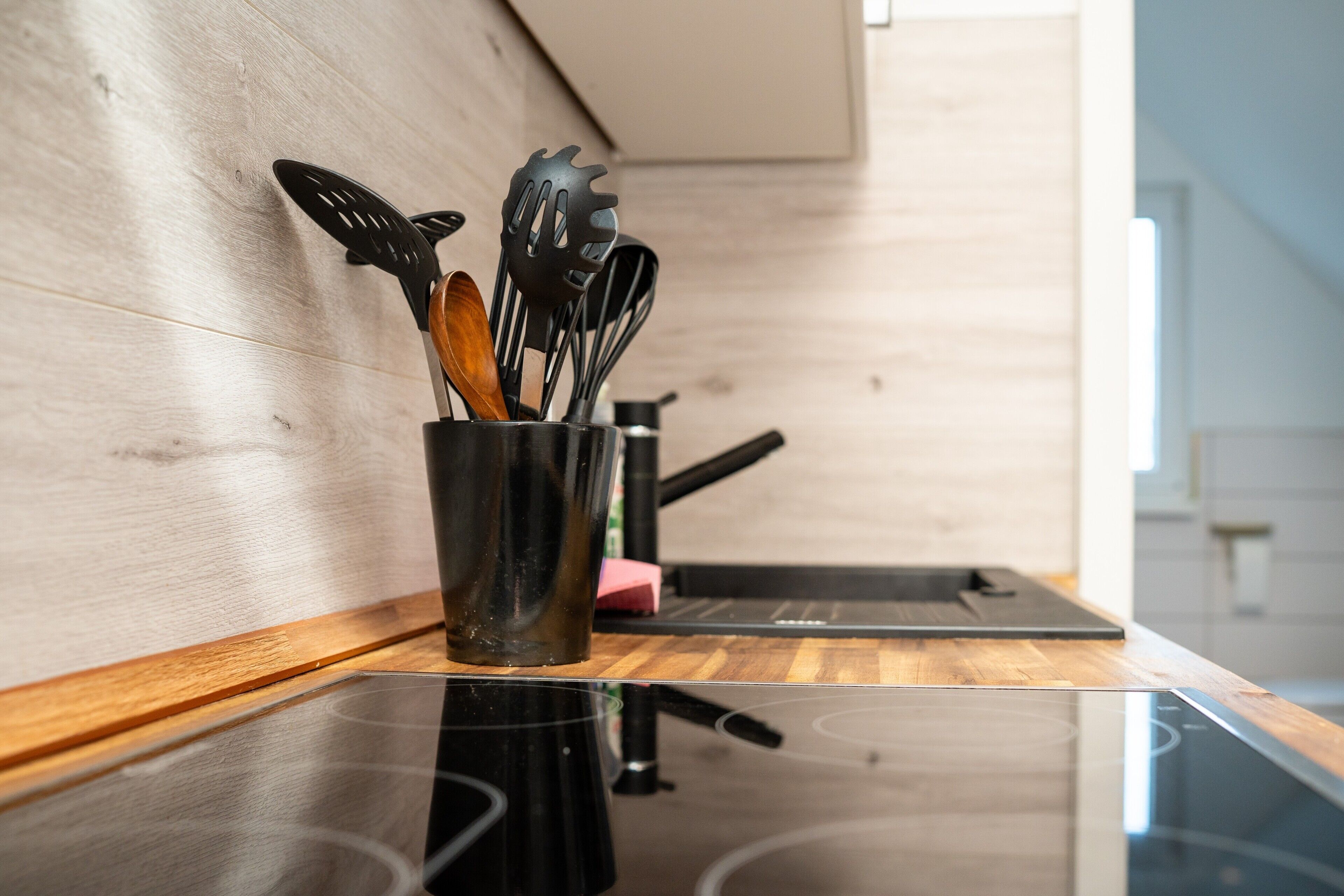 A kitchen with a wooden countertop, a black induction cooktop, and a utensil holder with various kitchen tools.