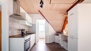 Eine schmale Küche mit Holzboden, weißen Schränken, einem eingebauten Backofen und einer Holzziel.