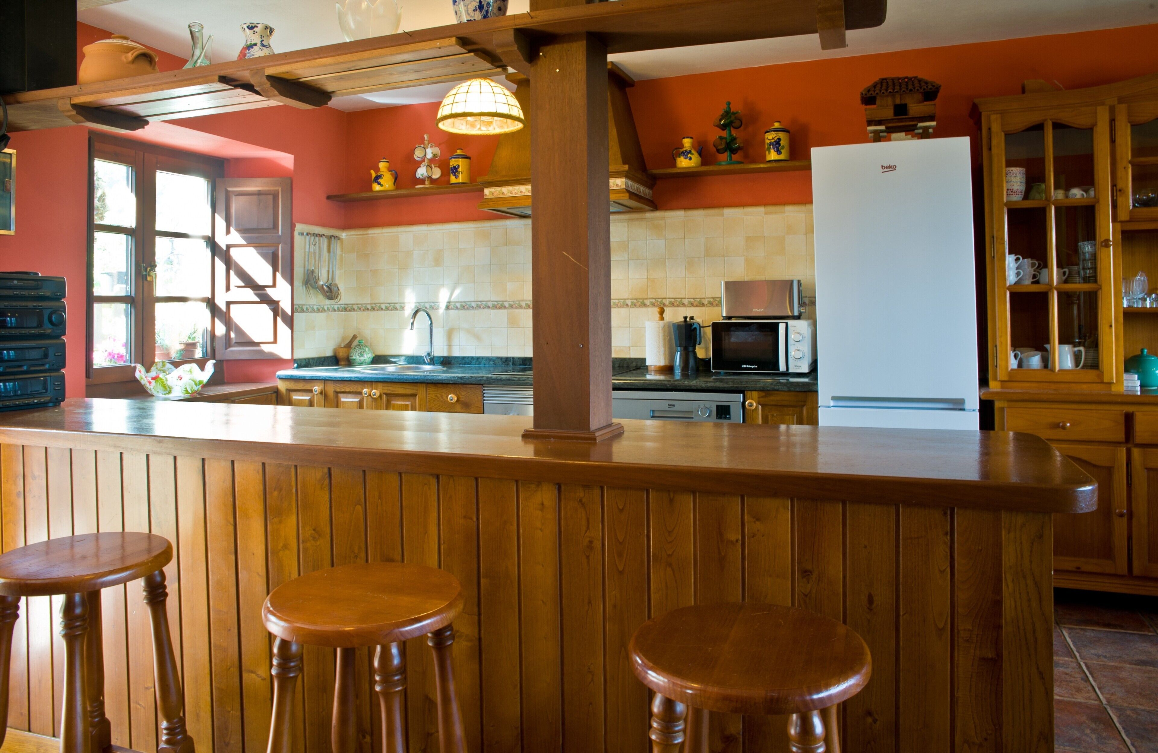 A kitchen with wooden bar stools, a refrigerator, a microwave, and a sink.