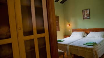 Una habitación con dos camas, una puerta de madera, una lámpara fijada a la pared y un cuadro enmarcado.