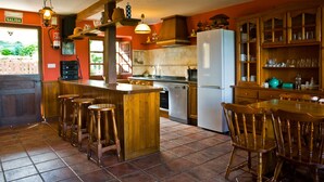 A kitchen with a bar area, wooden stools, a refrigerator, and a dining table with chairs. - Rural House 'Casa Remis' in Piloña – Sleeps 12, Private Bathrooms, Fireplace (Piloña)