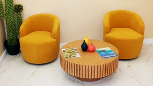 Una mesa redonda de madera con dos sillas amarillas, un cactus y algunas revistas.
