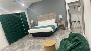 Una habitación de hotel moderna con una cama, mesitas de noche, un sillón de cuero y una pequeña mesa de madera.