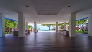 Terraza descubierta con piso de madera, pilares blancos y vista a una piscina y al océano.