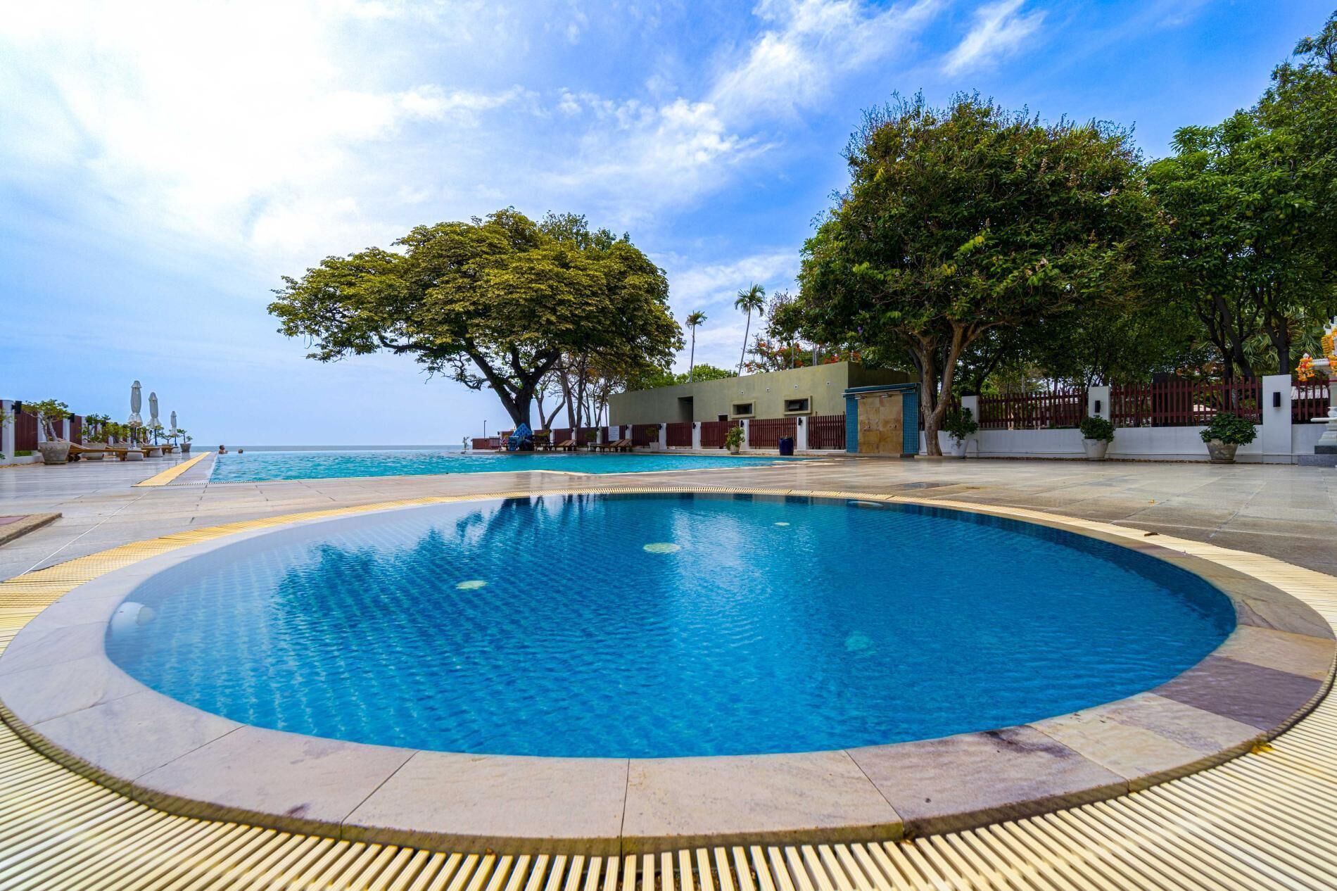 A circular infinity pool with a clear blue pool, surrounded by a tiled deck and a wooden deck with a yellow tactile path.