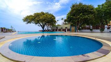A circular infinity pool with a clear blue pool, surrounded by a tiled deck and a wooden deck with a yellow tactile path.