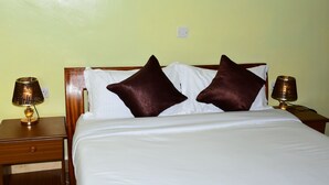 Cama bem arrumada com duas almofadas castanhas e lençóis brancos, com duas luminárias de cabeceira em mesas de madeira.