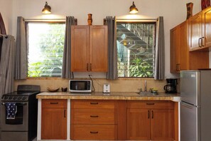 A compact kitchen with wooden cabinets, a stove, a microwave, and a refrigerator. - Villas el Parque 18A: Ocean-View Studio Apartment, Central, Pool, AC & WiFi (Quepos)