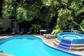 A swimming pool with a blue tiled edge, surrounded by lounge chairs and potted plants. - Villas el Parque 18A: Ocean-View Studio Apartment, Central, Pool, AC & WiFi (Quepos)