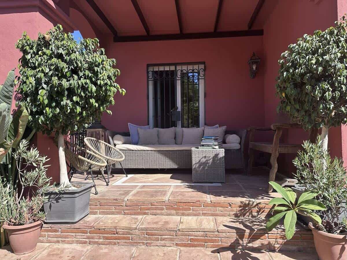An outdoor patio with a sofa, chairs, and potted plants.
