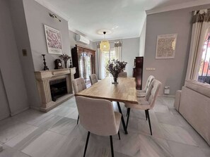 Ein Esszimmer mit einem langen Holztisch, sechs Stühlen, einem Kamin und einer Kristallleuchter.