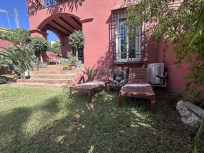 A patio with wooden furniture and a red building with a large window and a stone wall.