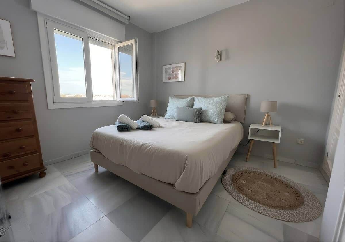 A bedroom with a bed, a dresser, a bedside table, a lamp, and a window.