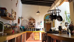 A kitchen with wooden cabinets, a stove, hanging pots, and a calendar on the wall. - El Diablo y la Sandia B&B (Oaxaca)