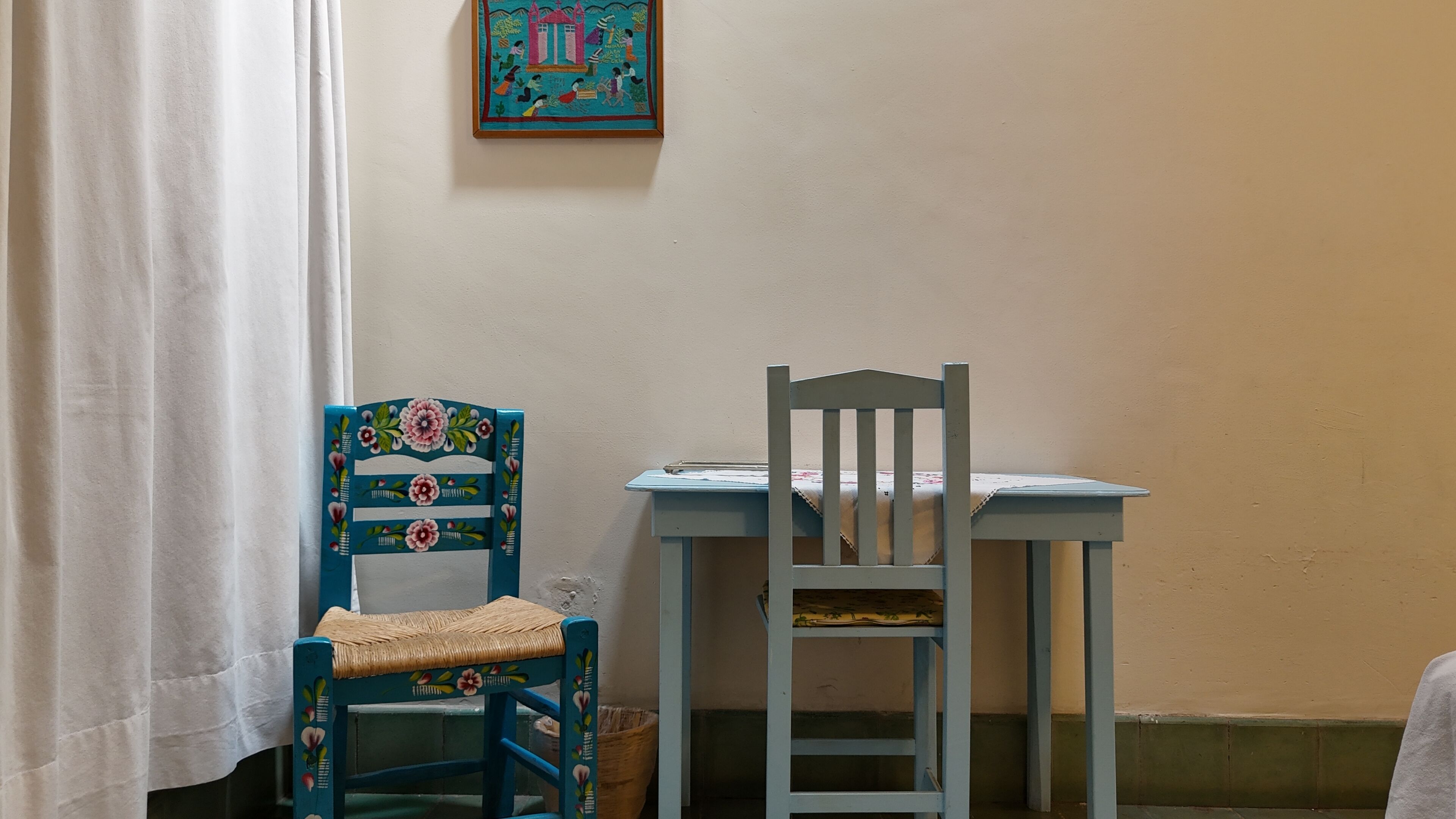 A room with a blue chair with a woven seat and a white table with a cloth.
