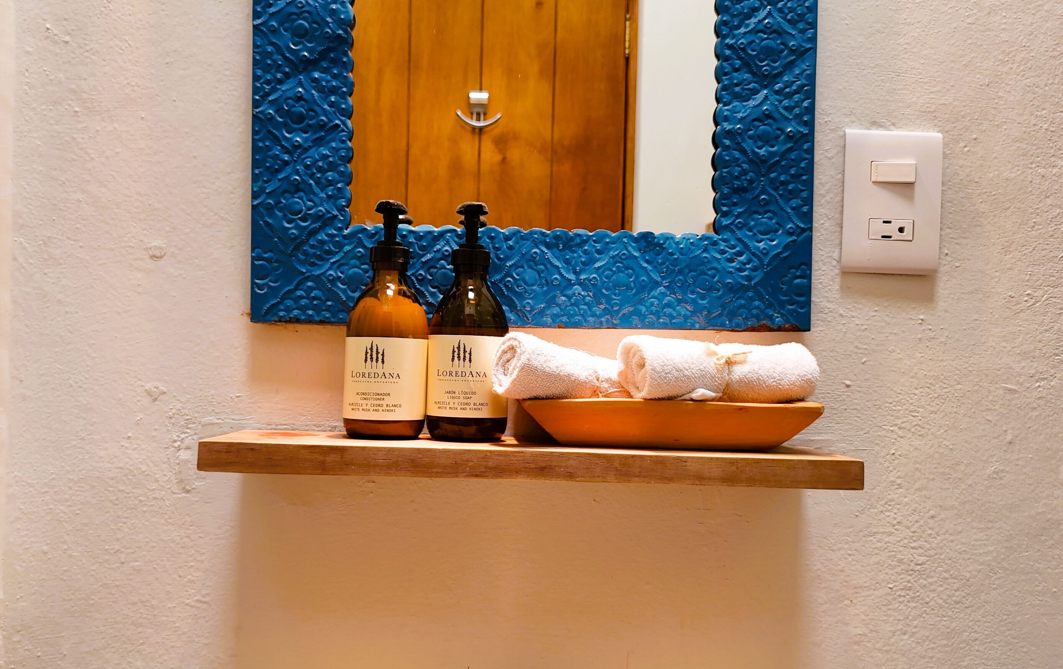 Ein Badezimmer mit einem hölzernen Regal, auf dem zwei Lotionflaschen und eine Schale mit weißen Handtüchern stehen.