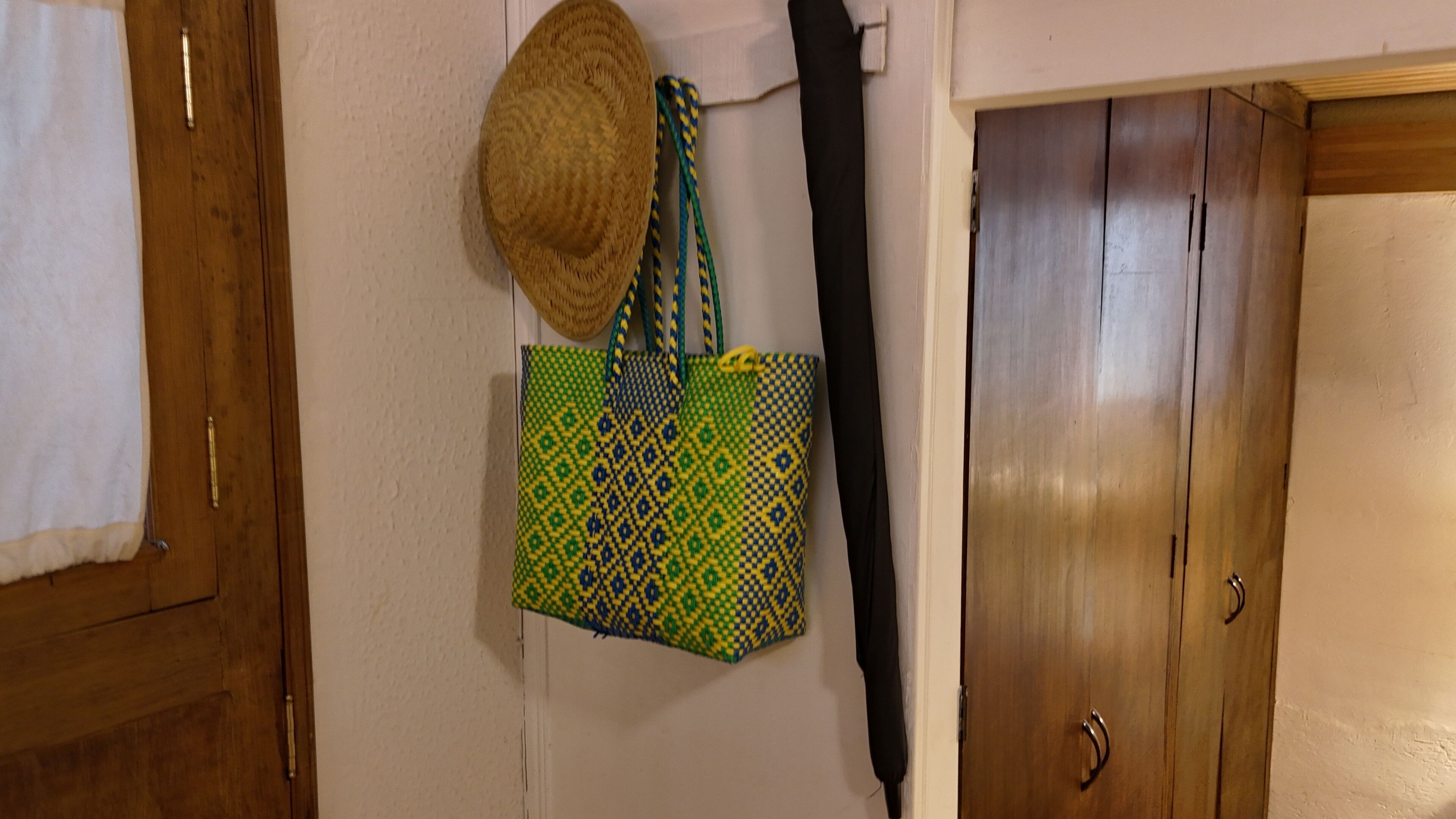 Eine Holztür mit einem Metallgriff, ein Strohhut an der Wand und eine Tasche mit einem grün-gelben Muster.