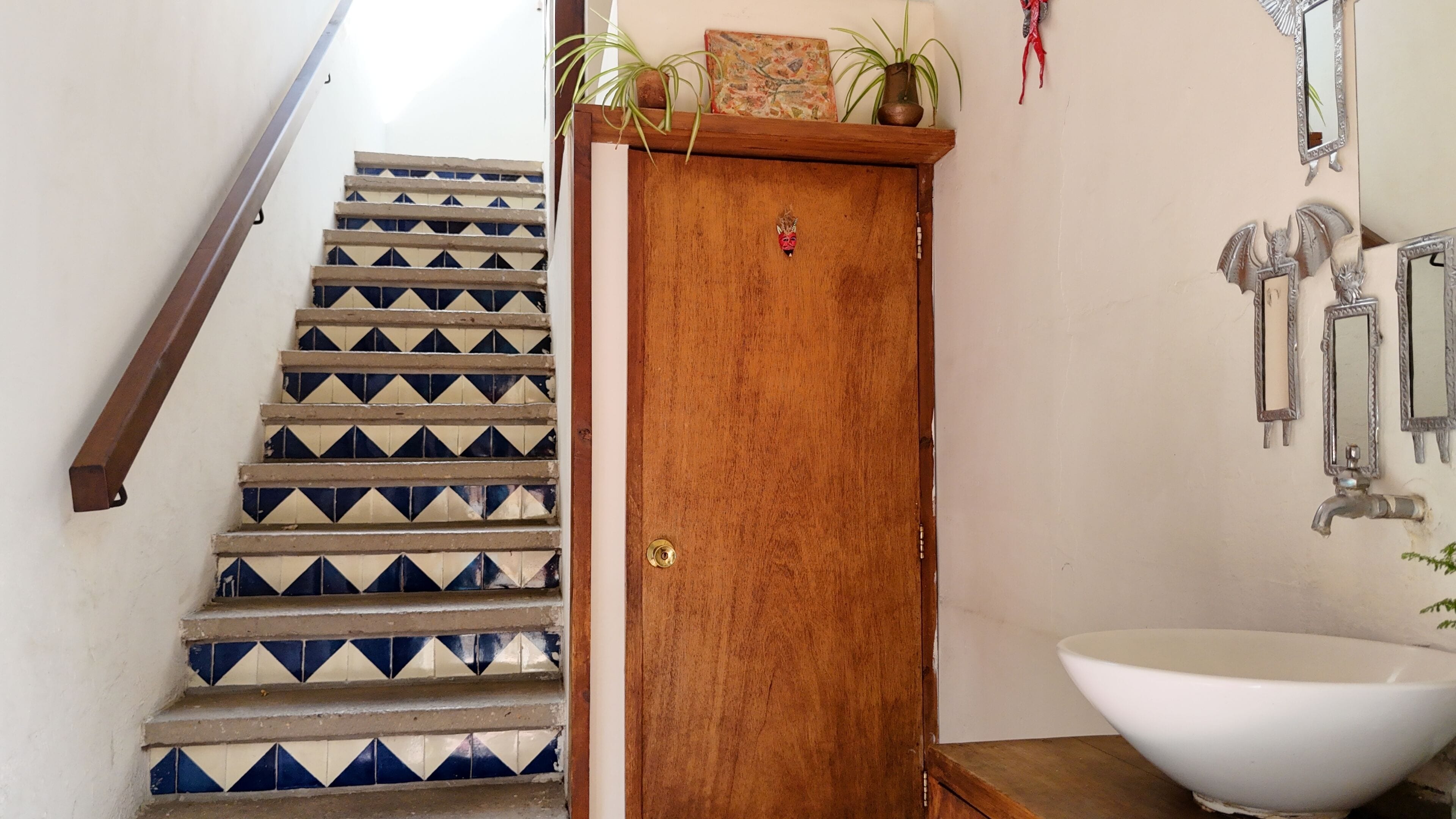 A staircase with patterned tiles, a wooden door, and a bathroom with a sink and mirrors.
