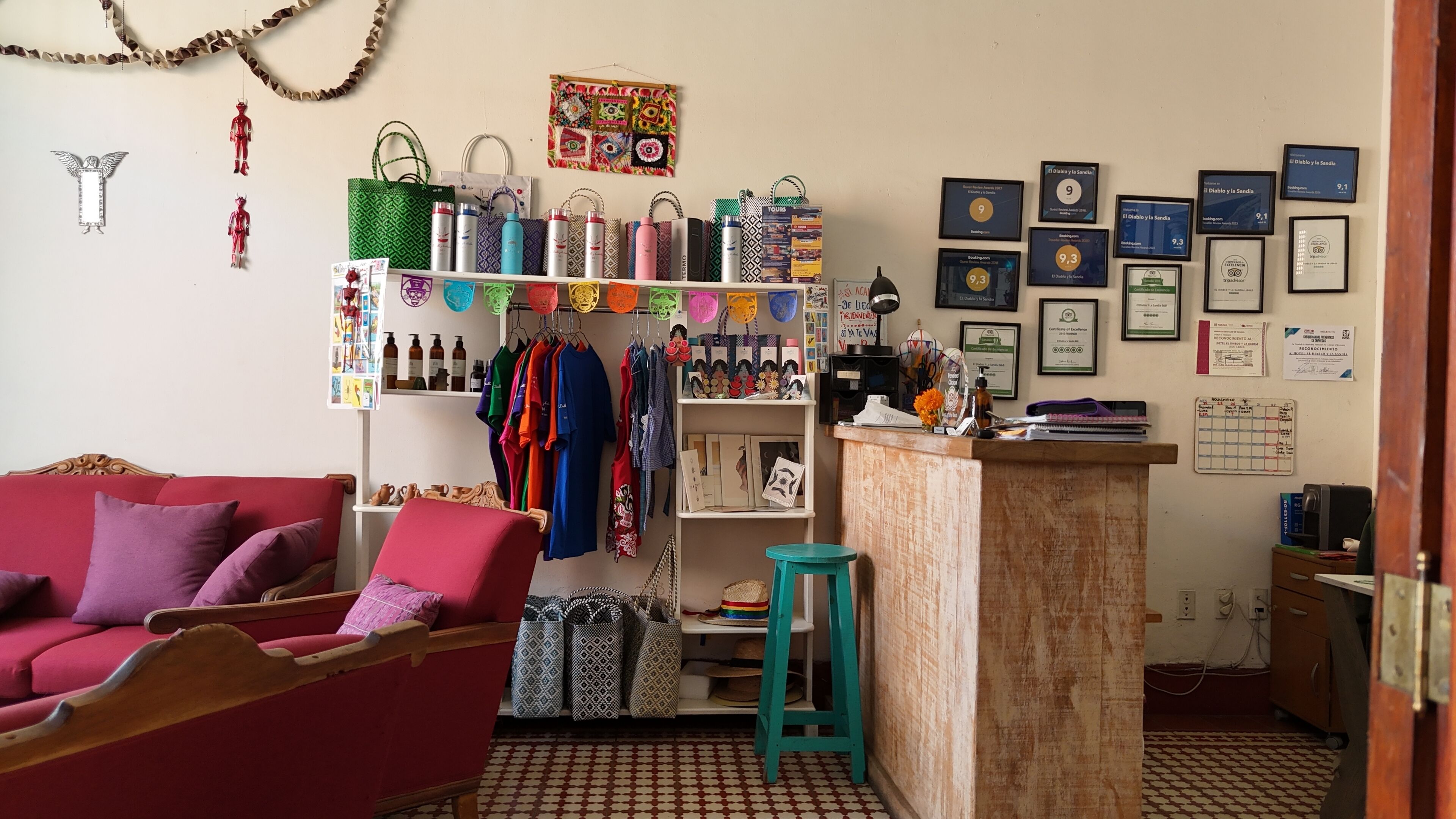 A cozy room with a red sofa, a wooden chair, a small table, and a shelf with various items including bags, bottles, and framed certificates.