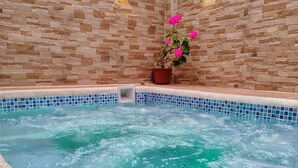 A spa area with a hot tub, stone walls, and two wall-mounted lights. - Suite San Vicente 1 Bathrooms Ecuador - Private Jacuzzi & Parking (Tungurahua)