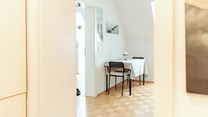 A room with a wooden floor, a dining table with chairs, and a white wall with a framed picture. - Lilians Cosy Apartment Jakomini 3B (Graz)