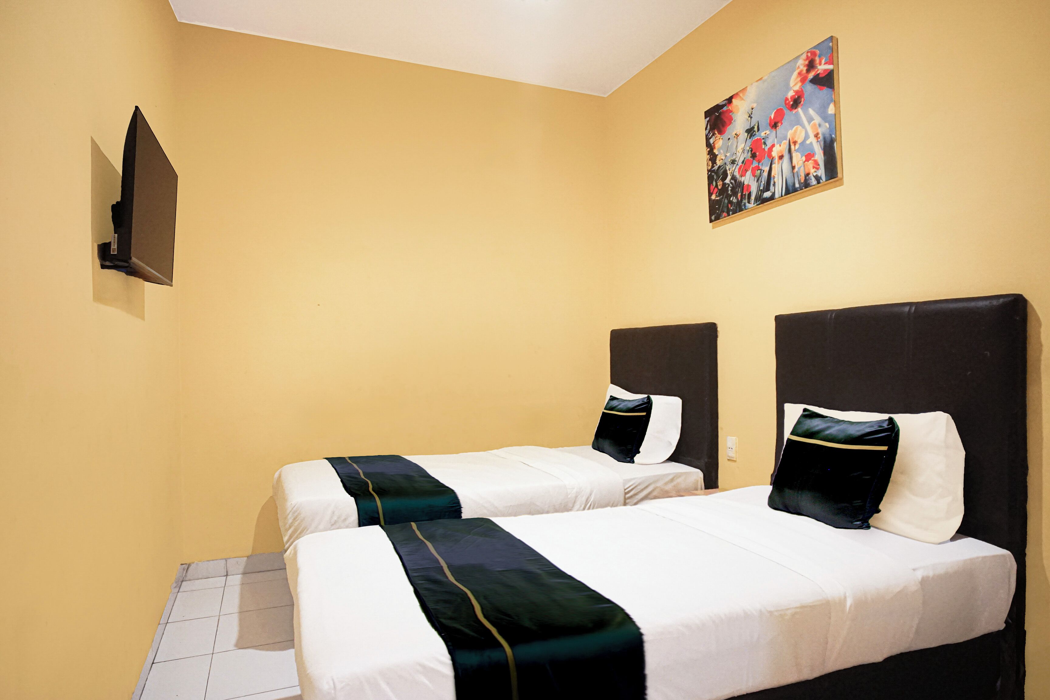A hotel room with two beds, a painting on the wall, and a flat-screen TV mounted on the wall.