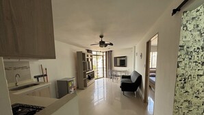Una cocina moderna con estufa integrada, un comedor con mesa y sillas, un sofá y un ventilador de techo.