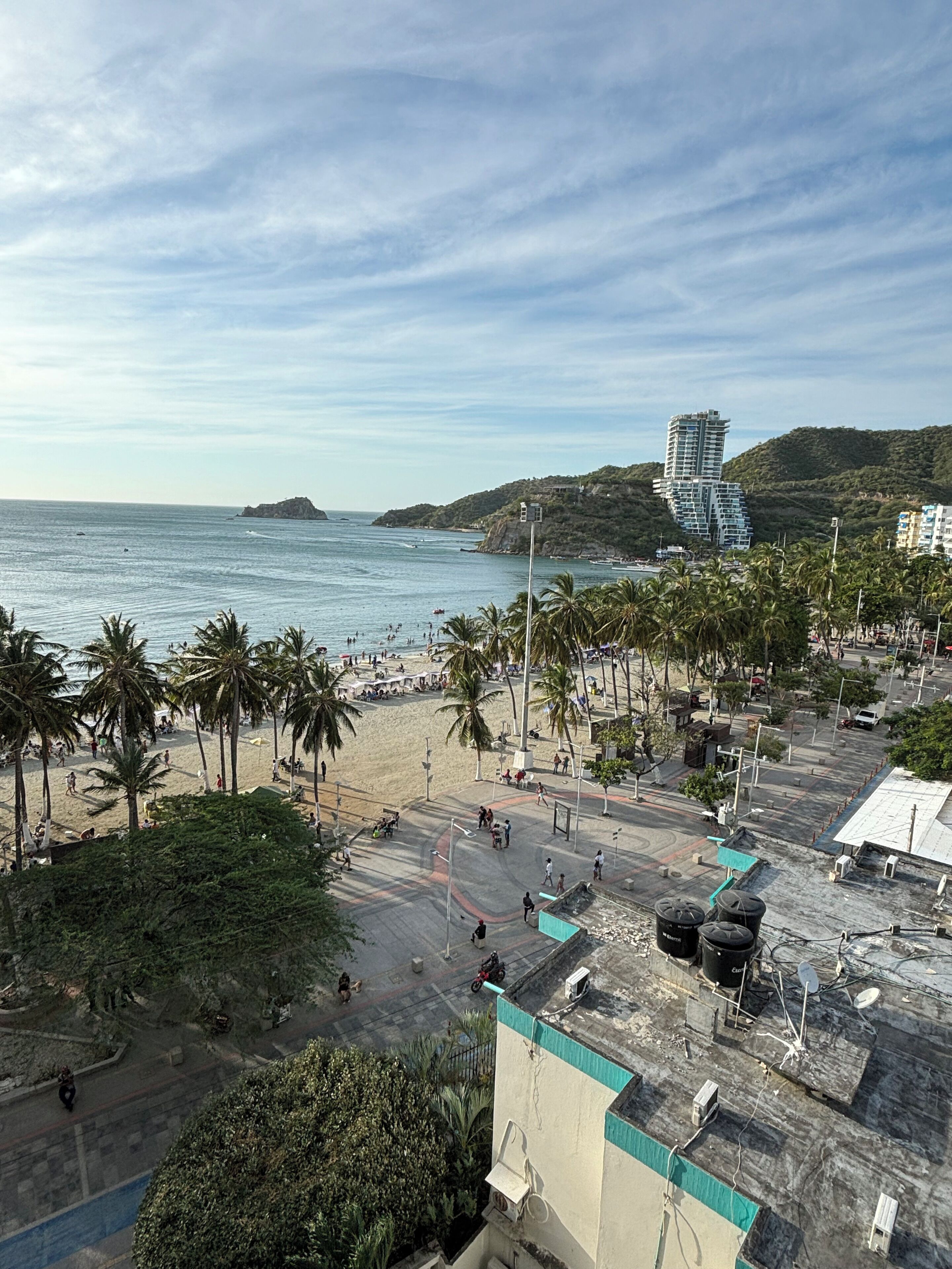 Uma área costeira com praia, palmeiras e um edifício moderno com design único.