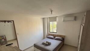 Un dormitorio con una cama, un escritorio de madera, un ventanal y un equipo de aire acondicionado.