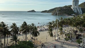 Una playa con palmeras, una orilla arenosa y un edificio moderno con balcones que dan al mar.