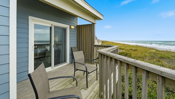 A wooden deck with chairs and a glass door leading to a room. - Charming Coastal-Facing 2-Bedroom Condo in Duck (Duck)