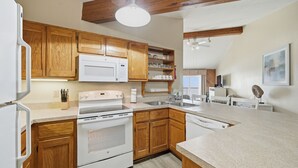 A kitchen with wooden cabinets, a white microwave, a stove, and a sink. - Charming Coastal-Facing 2-Bedroom Condo in Duck (Duck)