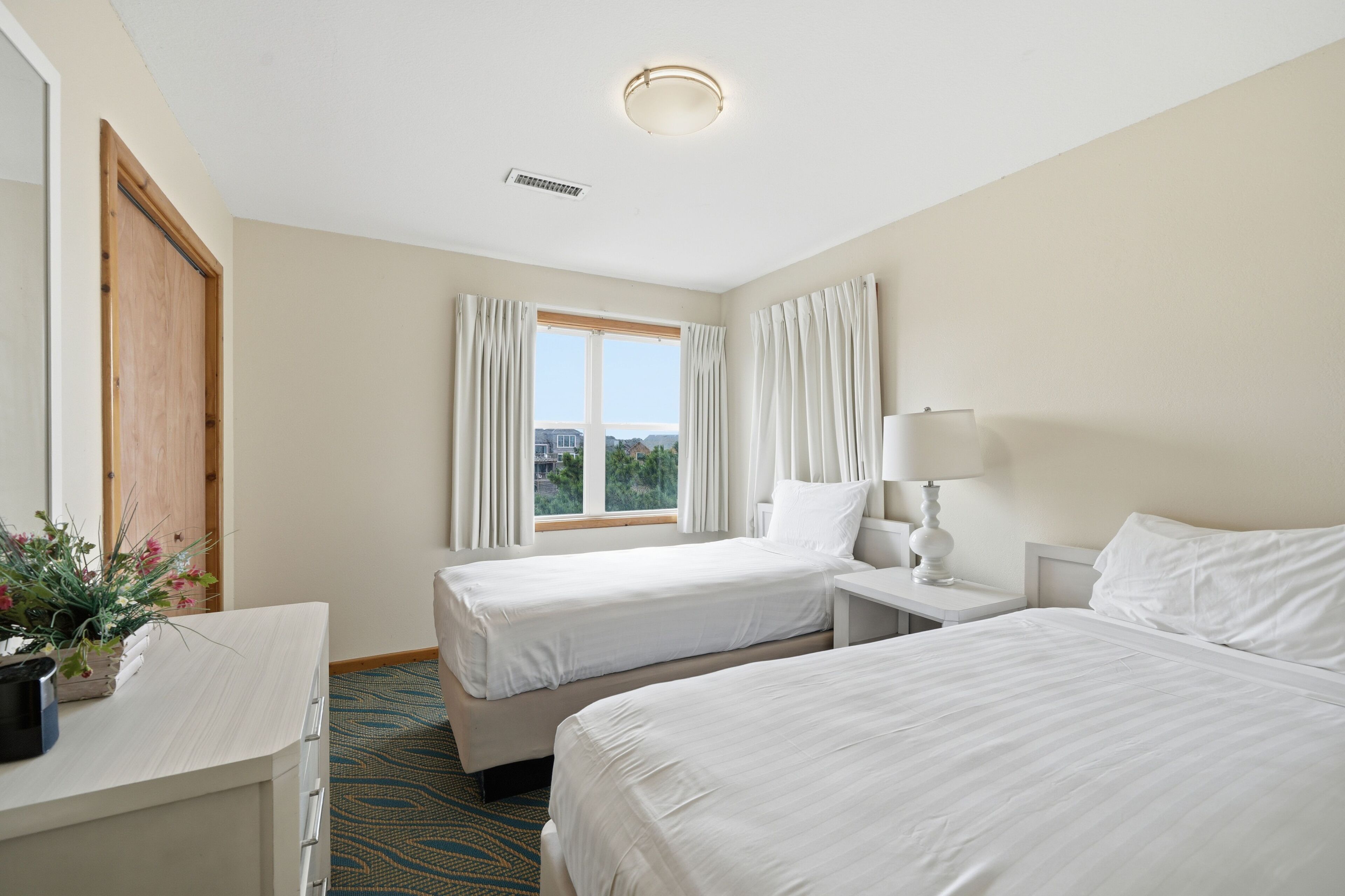 A hotel room with two beds, a desk, a lamp, and a window with curtains.