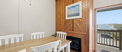A dining area with a wooden table and white chairs, a fireplace, and a view of the outside.
