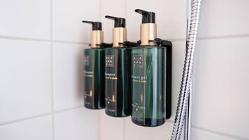 Un baño con ducha y cuatro botellas de champú y acondicionador en la pared.