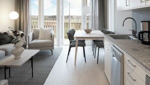 A modern living room with a sofa, a dining table, and a kitchen area with a dishwasher and a coffee maker. - Skerike Golfhus (Vasteras)
