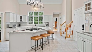 Una cocina amplia con una isla grande, muebles de cocina blancos y una lámpara moderna.