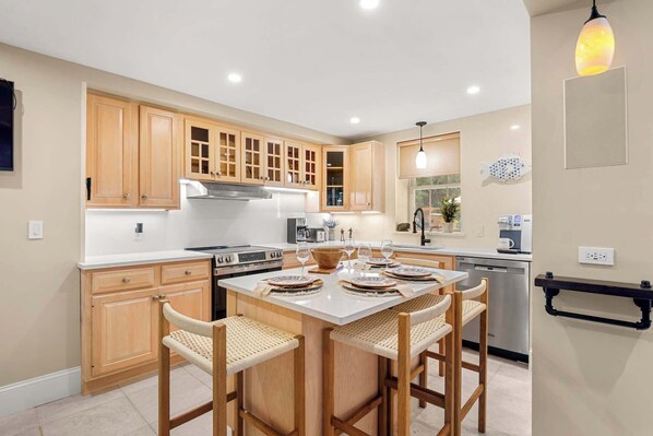 A modern kitchen with wooden cabinets, a central island with bar stools, a built-in oven, and a coffee machine. - Sprawling Home, Hot Tub, Walk to Main St! (Barnstable)