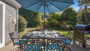 Patio esterno con tavolo apparecchiato per quattro persone, barbecue e un ombrellone grande.